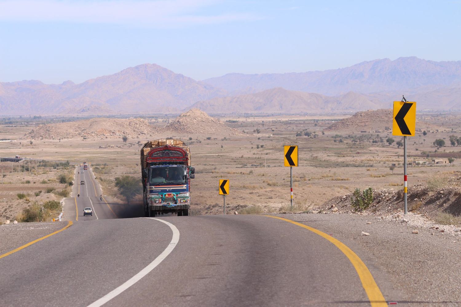 Colorful truck navigating a winding road in the arid mountains of Khuzdar, Pakistan.