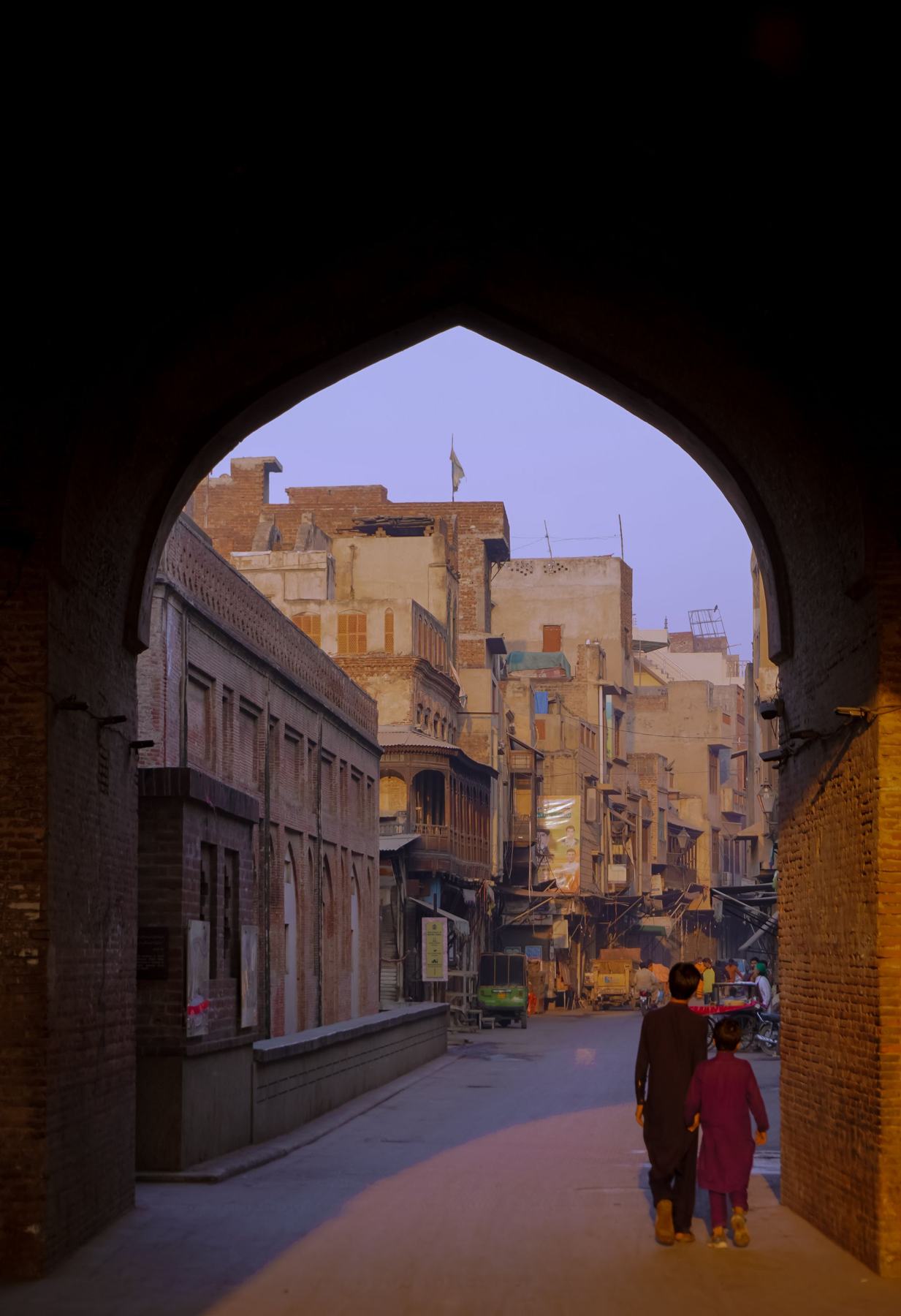 People walking through an arched gate into an old street at dusk